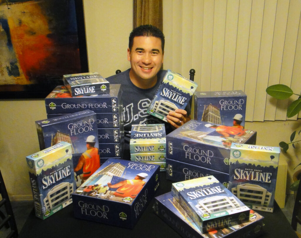 David Short sits at a table behind stacks of his board games.